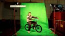A young man sits on his bike in front of a green screen.